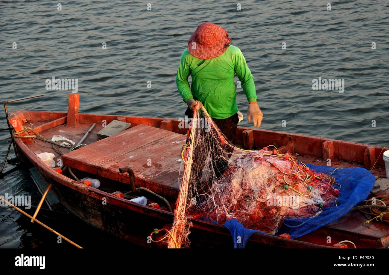 Bang Saen, Thailand: Thai fisherman hauling fishing nets into his small  skiff at the Bang Saen Sapan Pla pier Stock Photo - Alamy