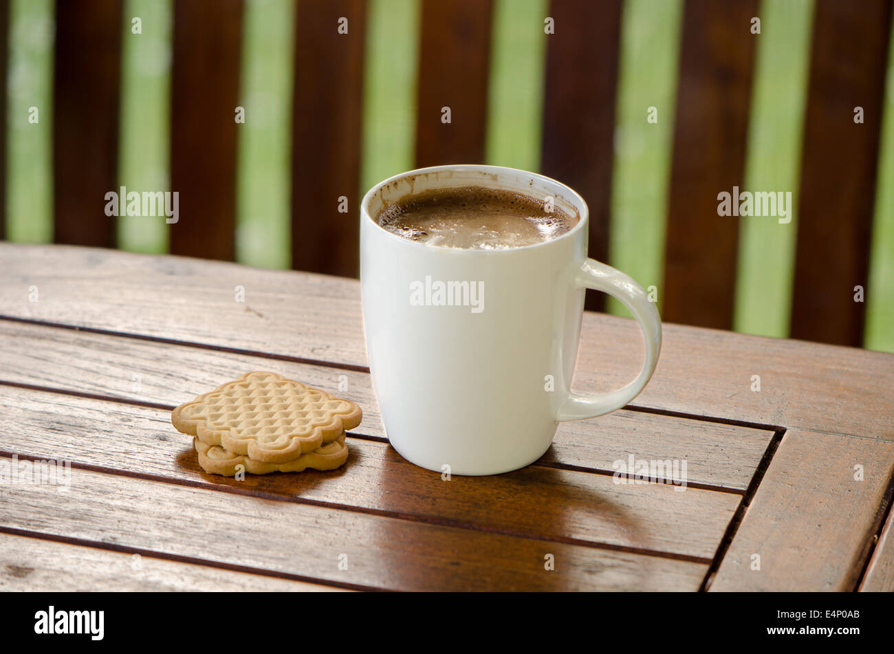 Cup of steaming hot coffee in white cup and cookie biscuit on table in outdoor bower. Stock Photo