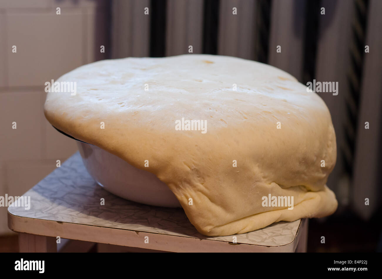 white yeast dough rise through the metal edges of the bowl Stock Photo