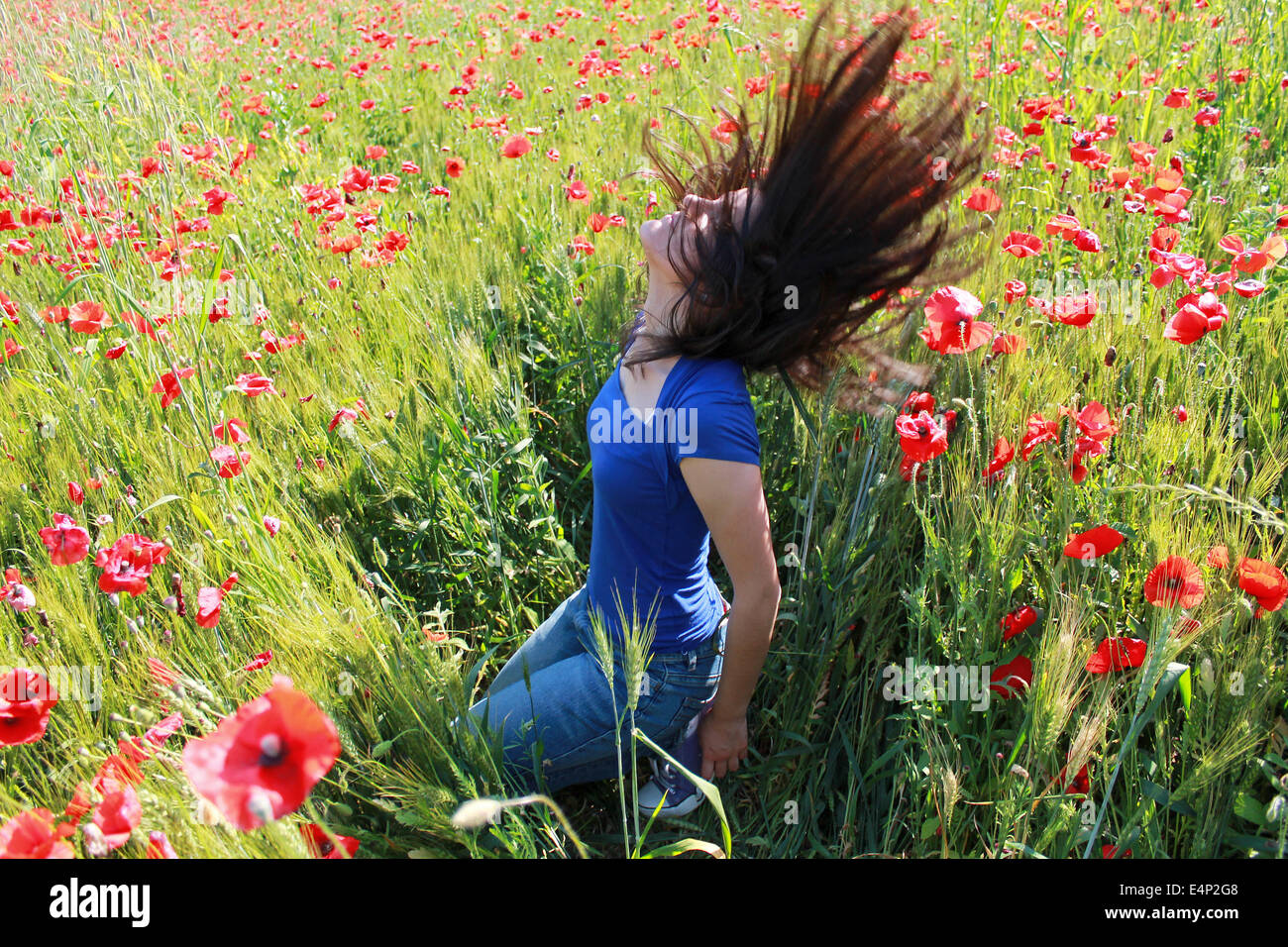 Teenage girl between red poppies playing with her long hair Stock Photo