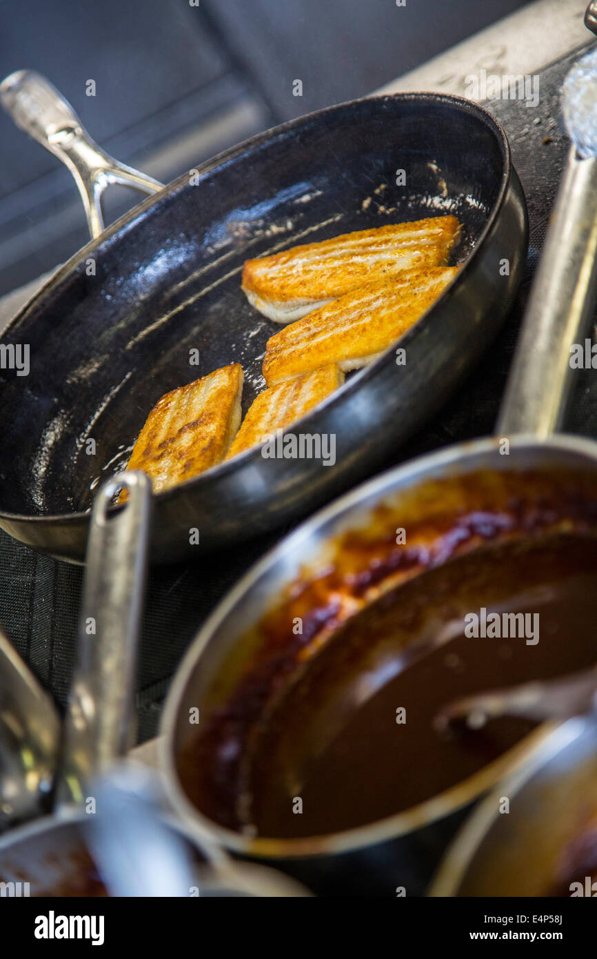 Kitchen of a restaurant, cooking pans and pots on an kitchen stove, fish fillet in a pan Stock Photo