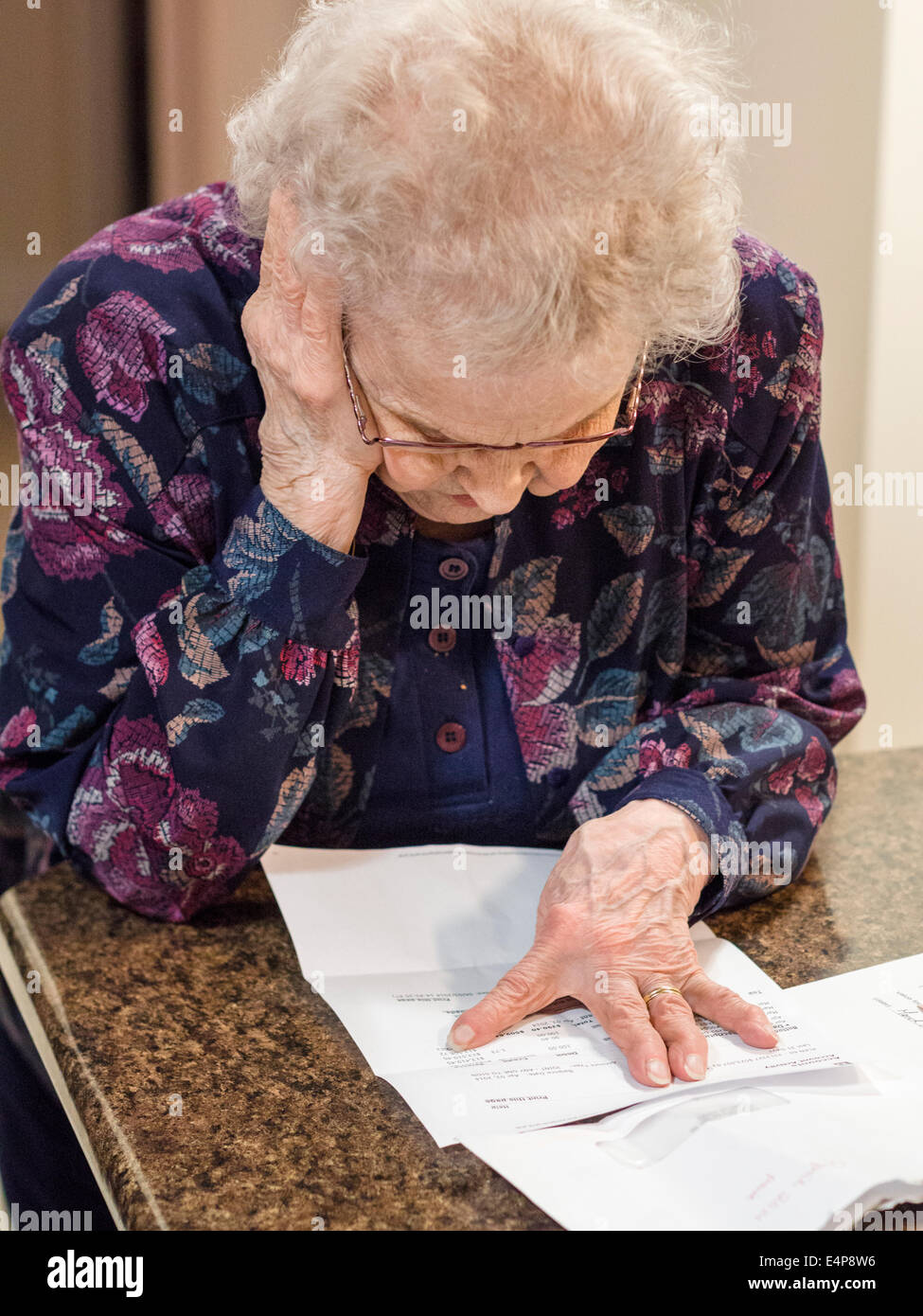 Trying to Understand a Letter. A senior woman reads a letter with her head held up by one hand while her other marks the words Stock Photo