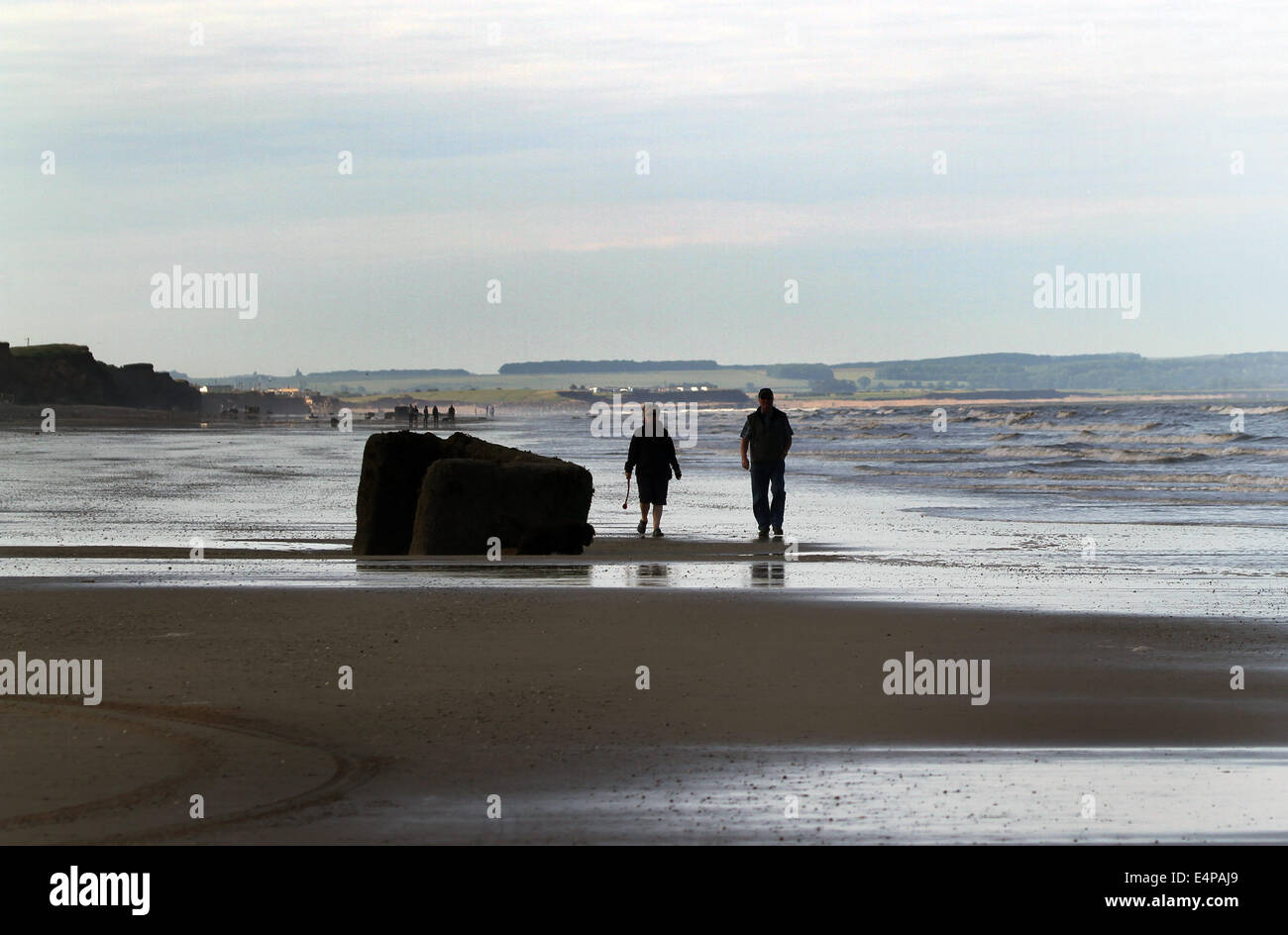Couple walking on beach at low tide. Stock Photo