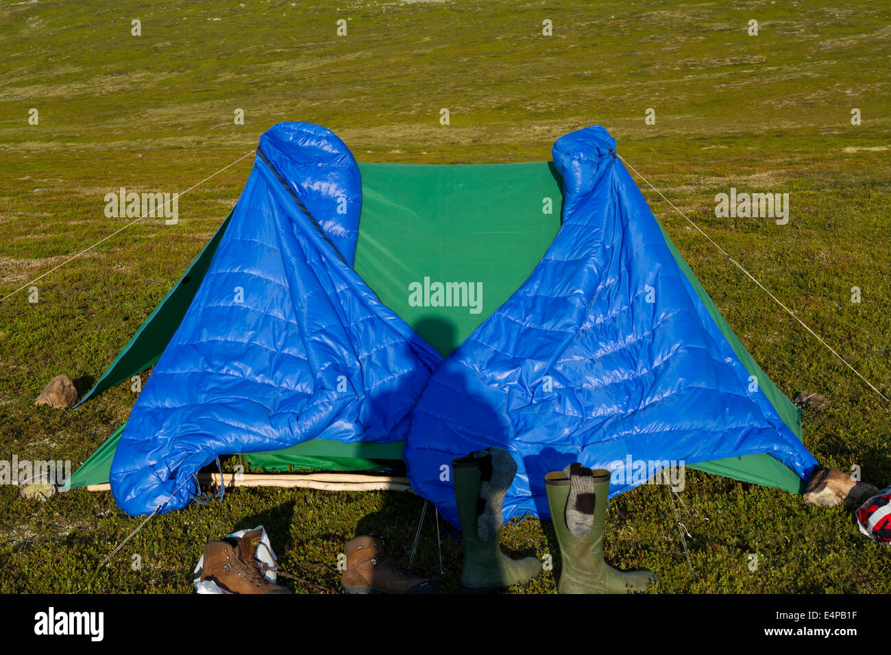 Shadow from a trekker on his tent with two sleeping bags hanging up to dry in the morning sun Stock Photo