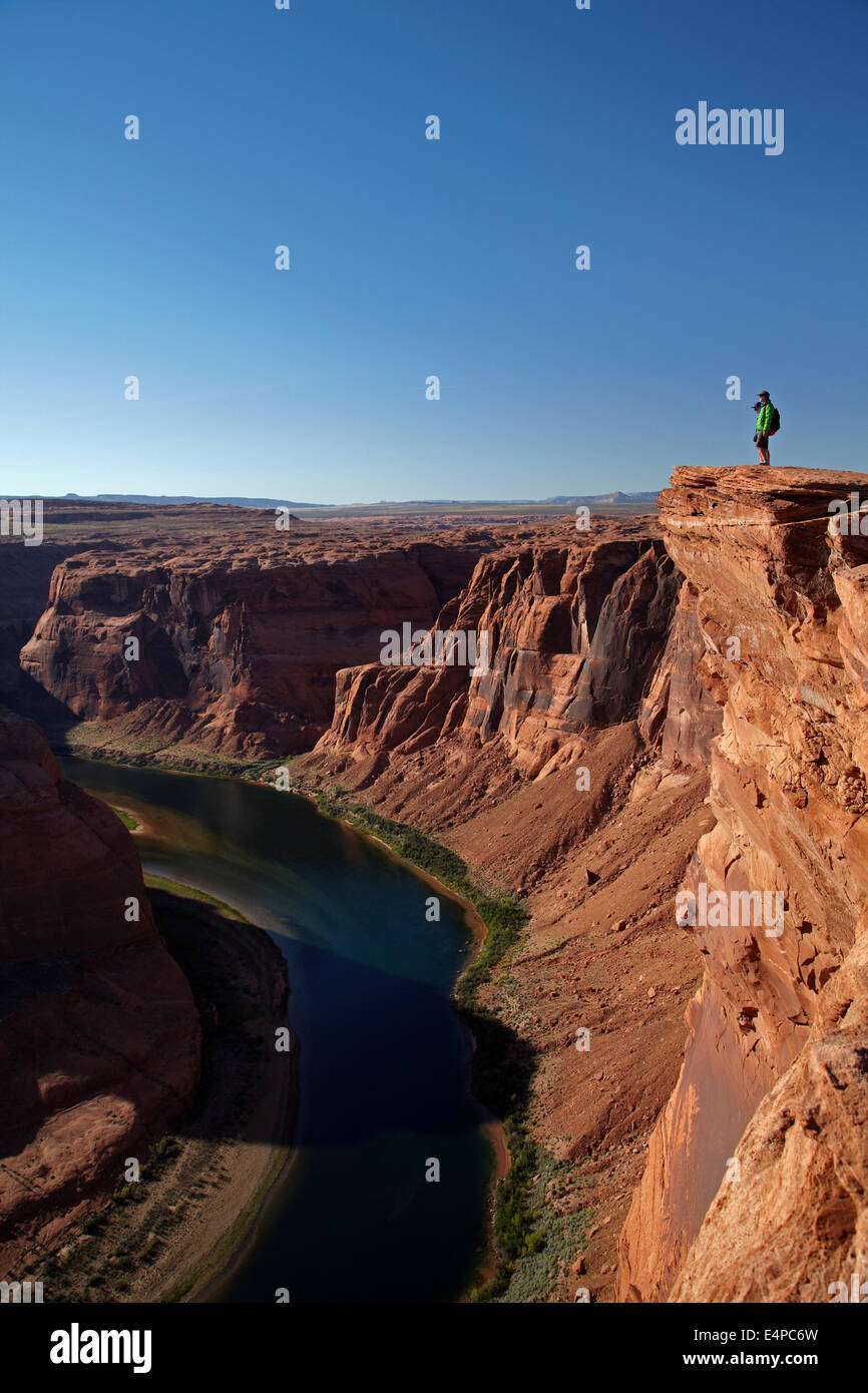 Tourist looking at 1000 ft drop down to Colorado River at Horseshoe Bend, just outside Grand Canyon, near Page, Arizona, USA Stock Photo