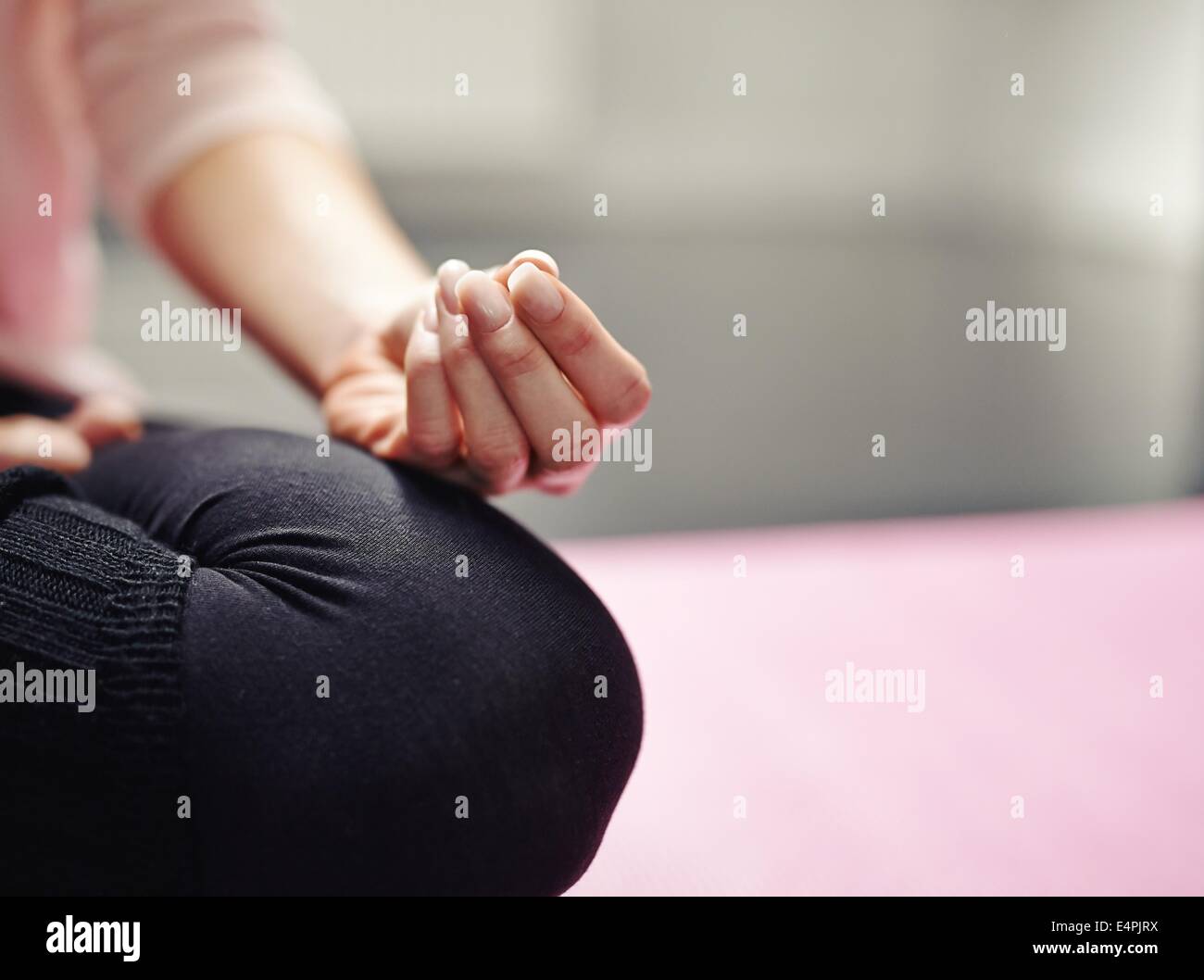Low section of woman sitting cross-legged on mat meditating in yoga posture. Cropped image of woman practicing yoga with focus o Stock Photo