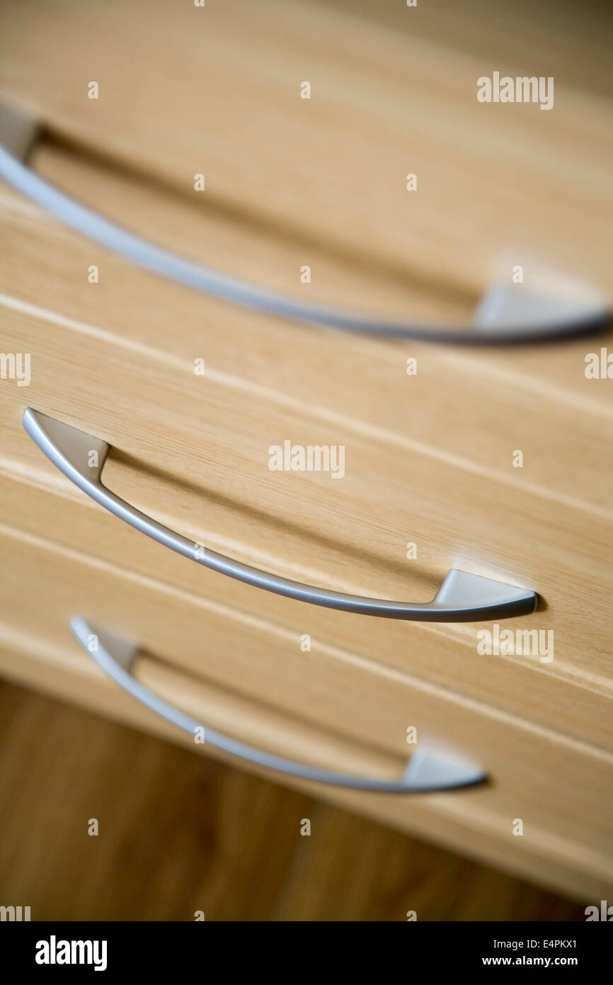 contemporary drawer handles in silver metal on light coloured wood veneer drawers. Stock Photo