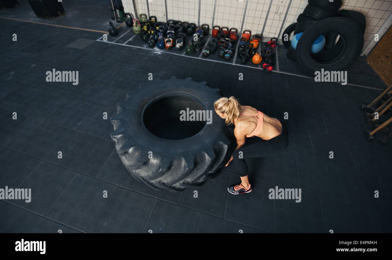 Top view of young female flipping heavy tire. Woman doing crossfit workout at gym. Stock Photo