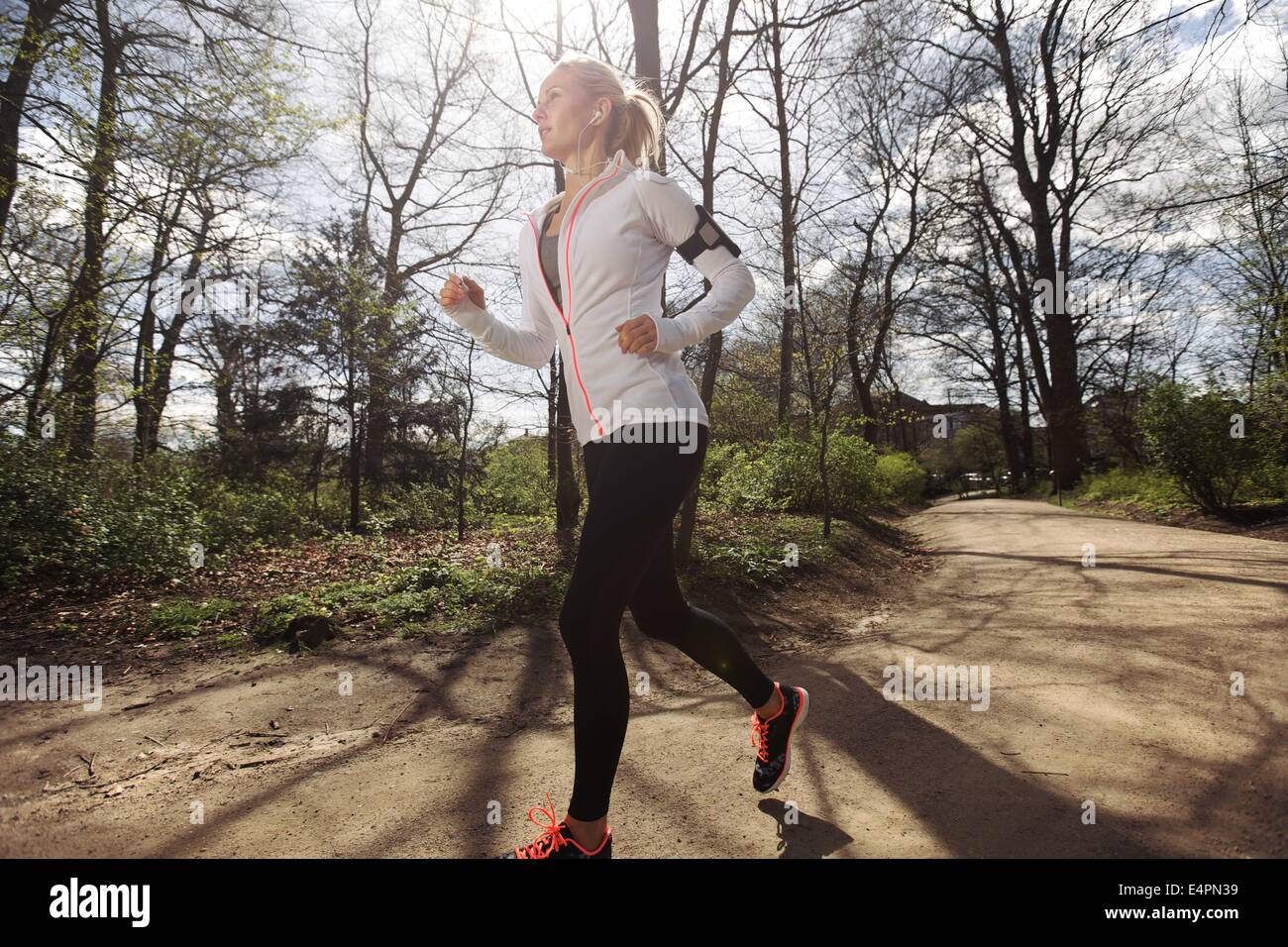 Fitness woman running in park on summer day. Caucasian female runner during outdoor workout. Fit female model jogging in forest. Stock Photo