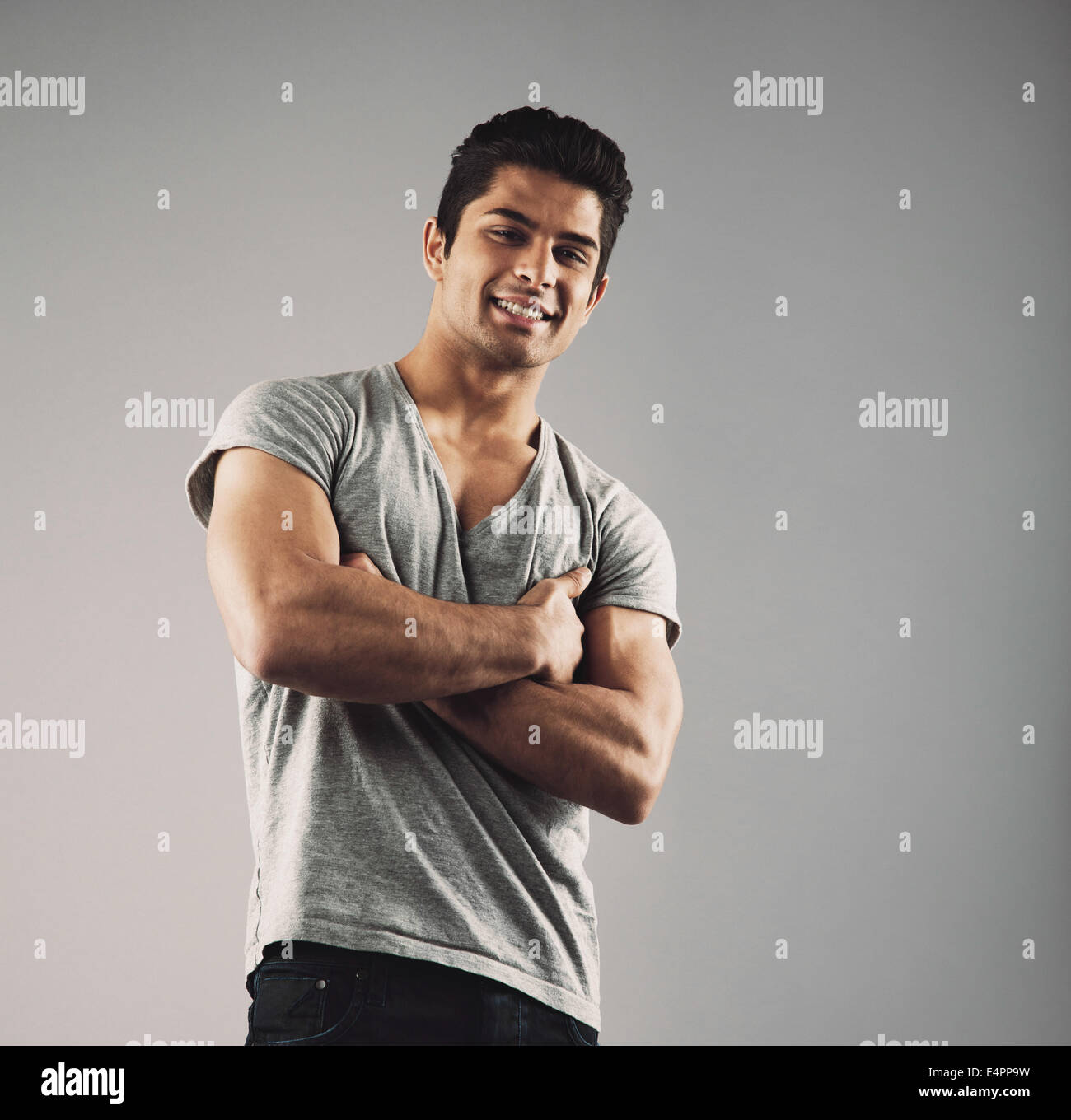 Portrait of smart young muscular man posing against grey background. Happy young hispanic male model standing with his arms cros Stock Photo