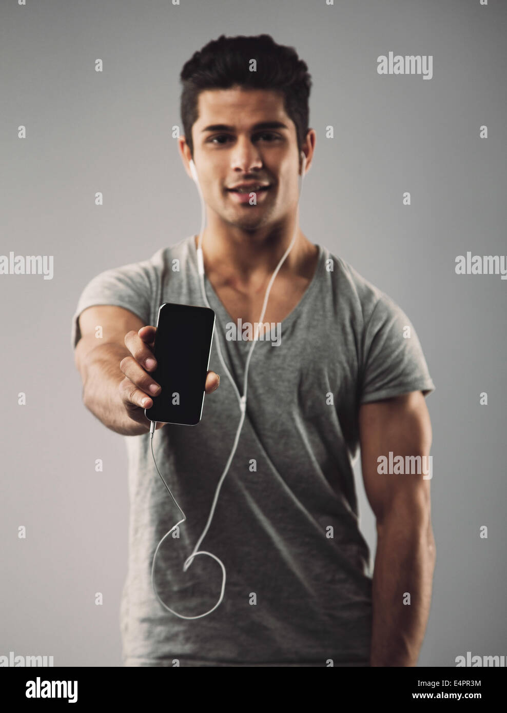 Young man wearing earphones showing his new mobile phone. Hispanic male ...
