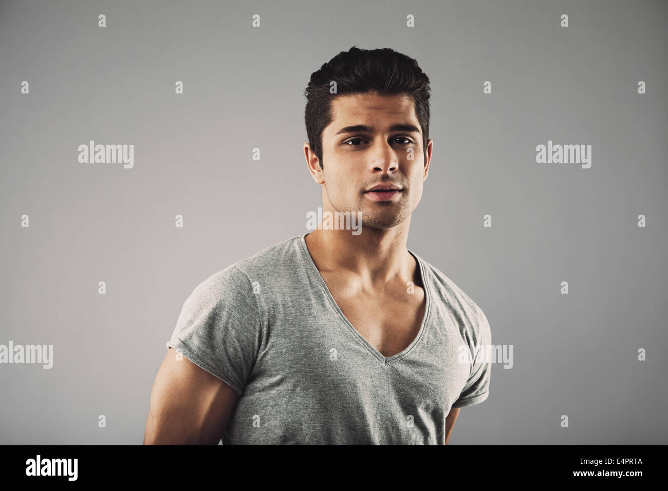 Portrait of handsome young man looking at camera. Hispanic male fashion model posing against grey background. Stock Photo