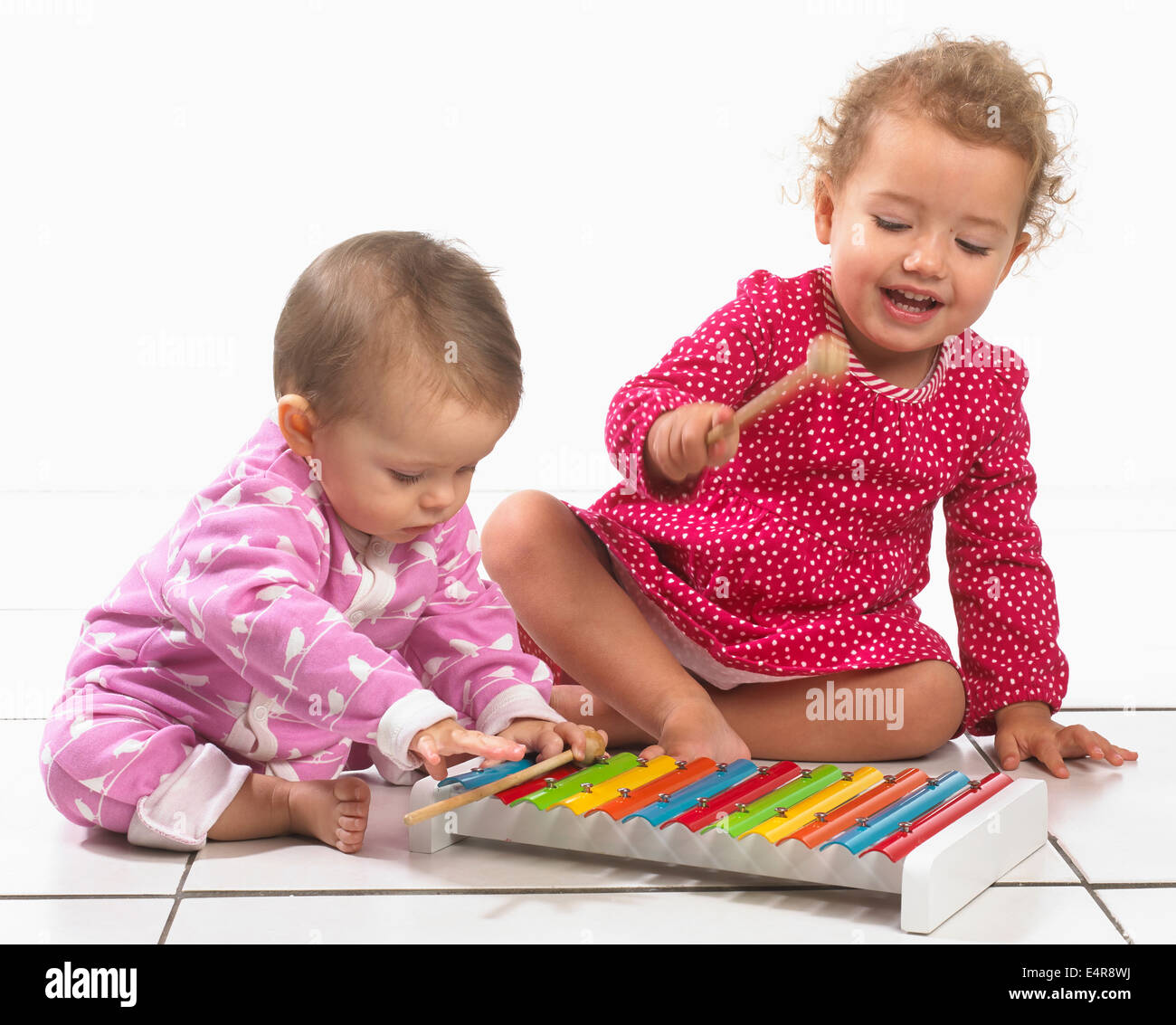 Baby girl (8 months) and young girl (2 years) playing with colourful toy xylophone Stock Photo