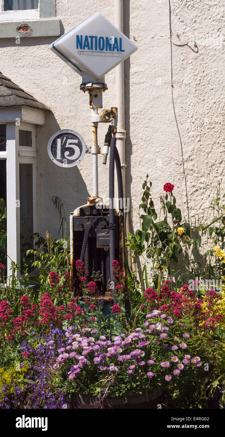 An old petrol pump decorating a garden at Ravenglass, Cumbria, UK. The price shows 1 shilling and 5 pennies (approx 8p). Stock Photo