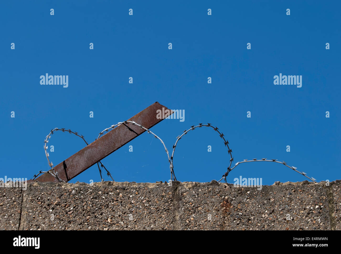 concrete wall topped by barbed wire, seen against a blue sky Stock ...