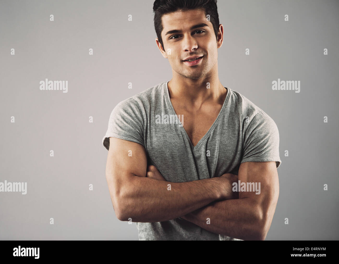Cropped image of muscular young man standing with his arms crossed against grey background. Macho man posing confidently. Stock Photo