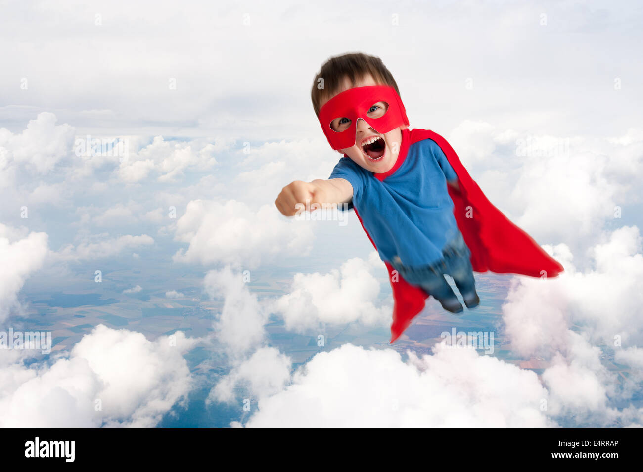 superhero boy child flying upwards in the sky through the clouds Stock Photo
