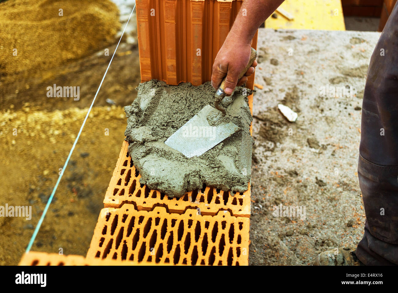 Anonymous construction worker on a building site with the building of a house establishes a wall from brick. Brick wall of a mas Stock Photo