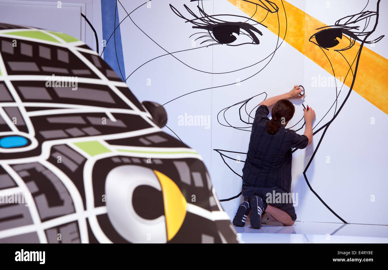 Berlin, Germany. 16th July, 2014. A conceiled Smart car is pictured on a white platform at Tempodrom in Berlin, Germany, 16 July 2014. In the backgrund artist El Bocho works on the portrait of a woman. The 'fortwo' with two seats and the 'fourfour' with four seats will be presented in the evening. The cars will be introduced on the market on 22 November 2012. Photo: Soeren Stache/dpa/Alamy Live News Stock Photo