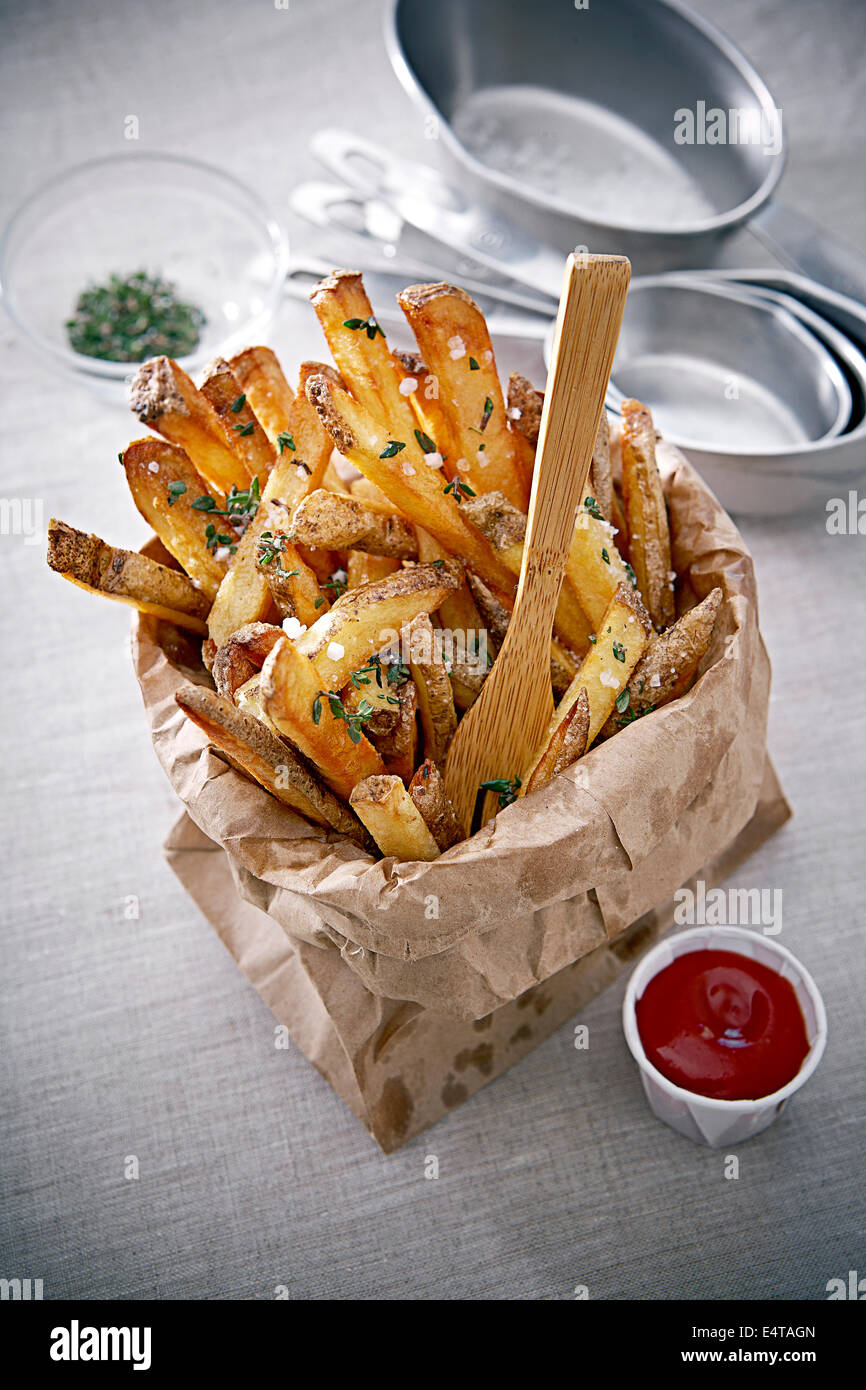 Seasoned French Fries in Paper Bag with Wooden Fork and Ketchup, Studio Shot Stock Photo