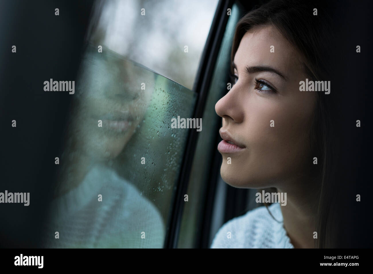 Portrait of young woman sitting inside car and looking out of window and day dreaming on overcast day, Germany Stock Photo