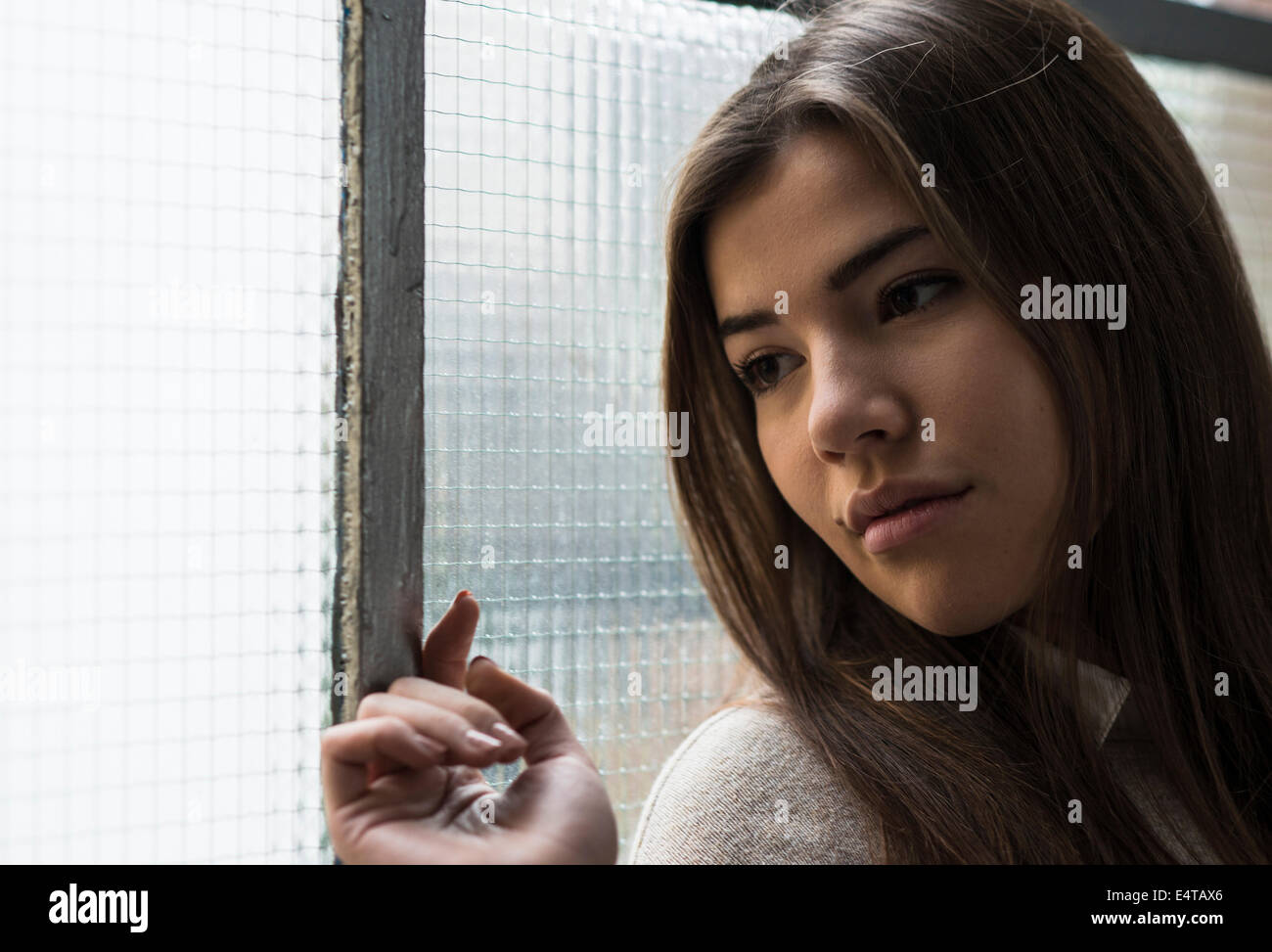 Close-up portrait of young woman standing in front of window, day dreaming and looking into the distance, Germany Stock Photo