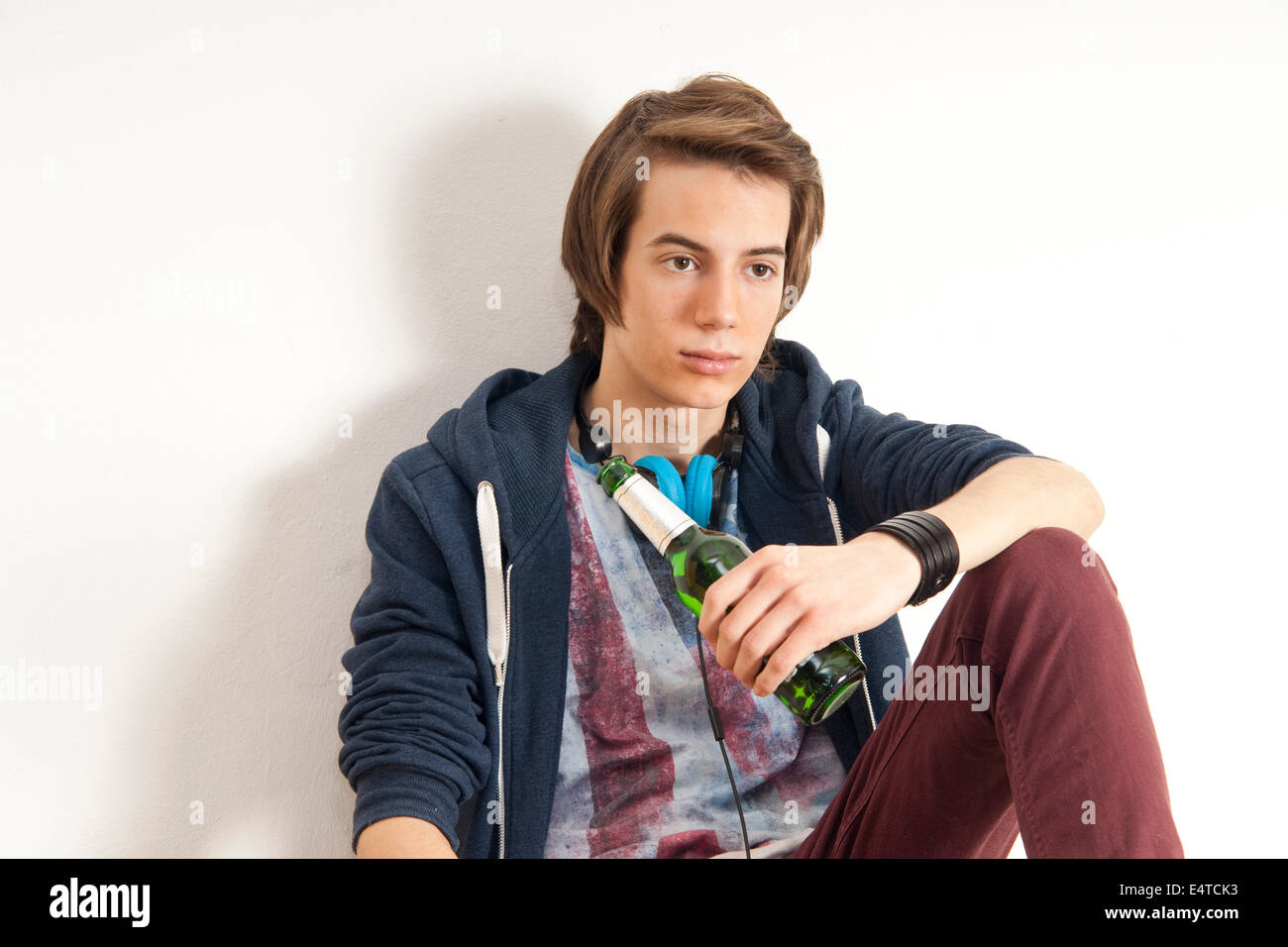Teenage boy wearing headphones around neck and holding bottle of beer, studio shot on white background Stock Photo