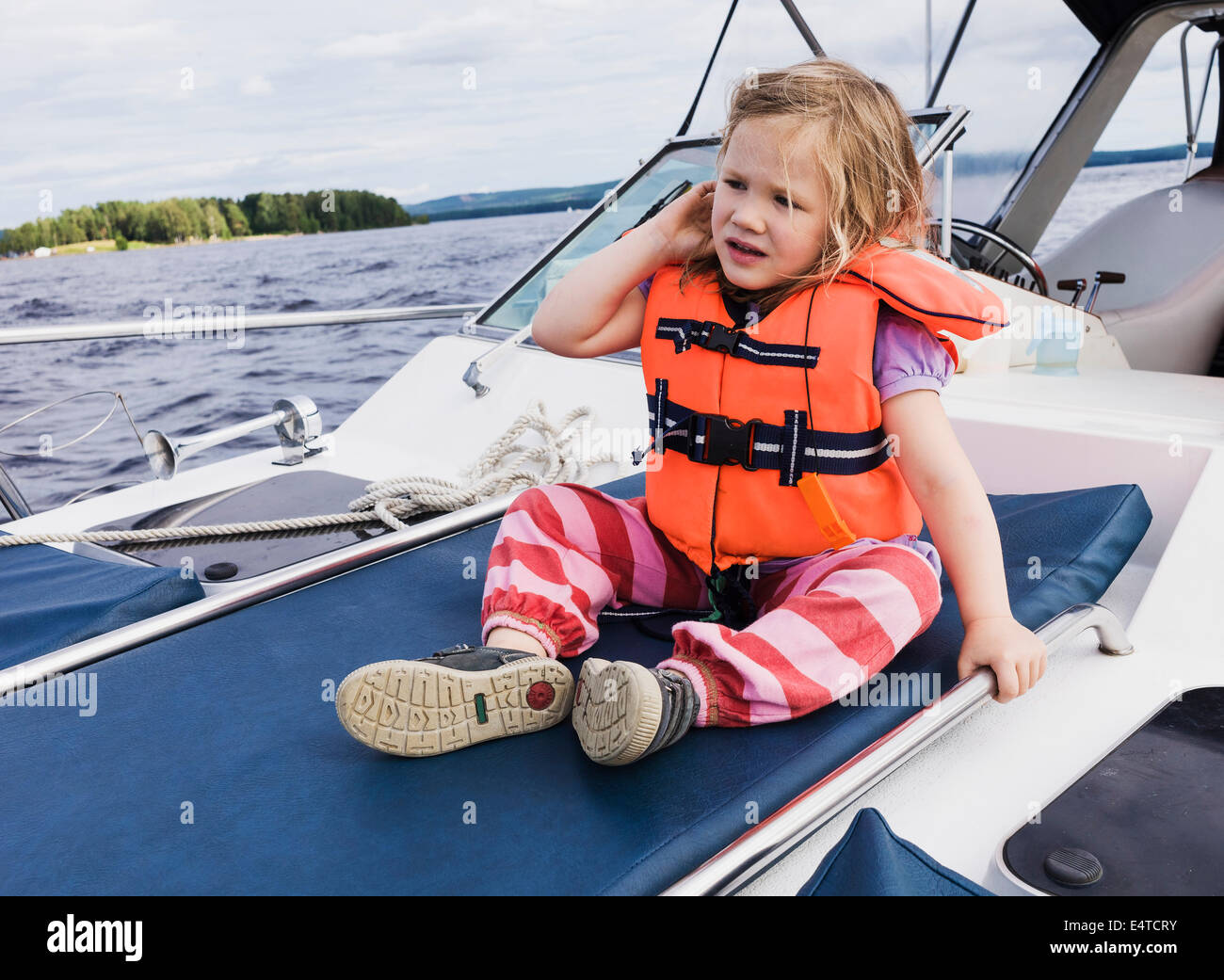 3 year old girl in orange life jacket sitting on top of motorboat, Sweden Stock Photo