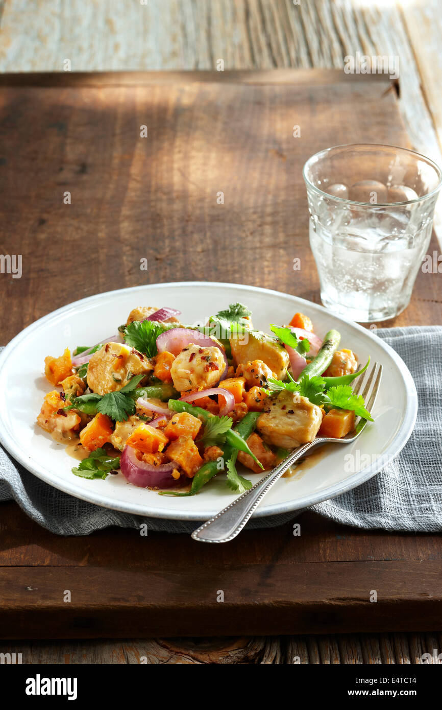 Peanut chicken stir fry with red onions, green beans, carrots, cilantro and hot peppers on plate with fork and a glass of water Stock Photo