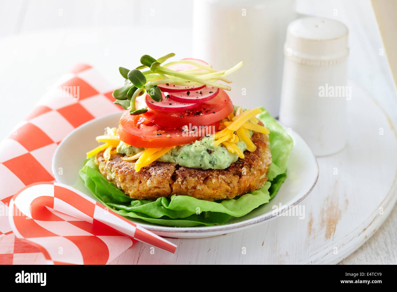 Gluten free chickpea burger with lettuce, guacamole, shredded cheddar cheese, tomatoes, red onion, and sprouts Stock Photo