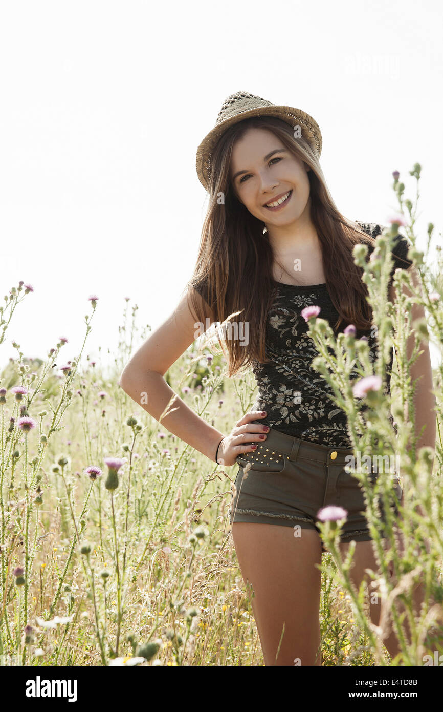Portrait of teenage girl wearing shorts and straw hat standing in field, smiling and looking at camera, Germany Stock Photo