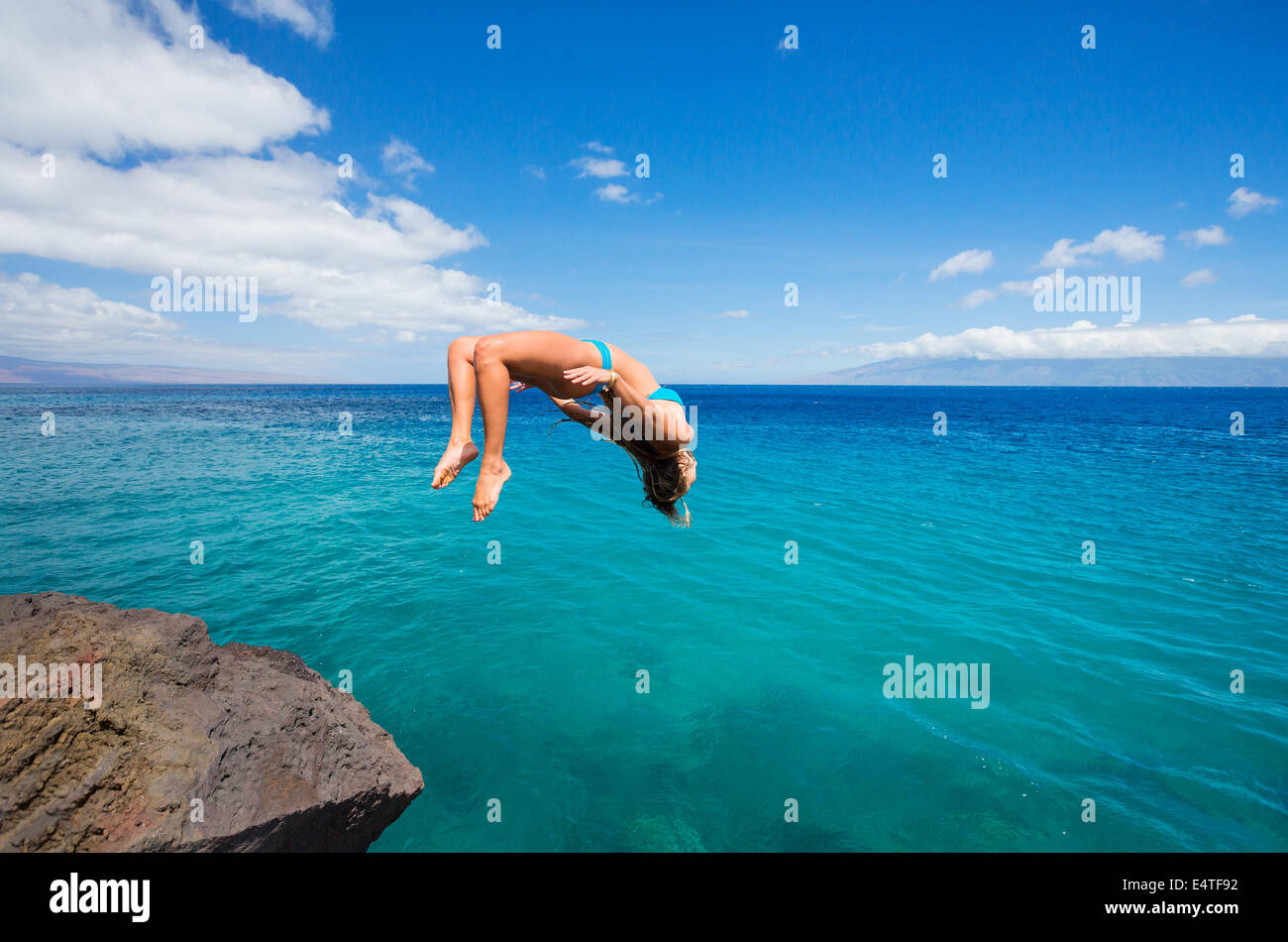Woman doing backflip off cliff into the ocean. Summer fun lifestyle. Stock Photo