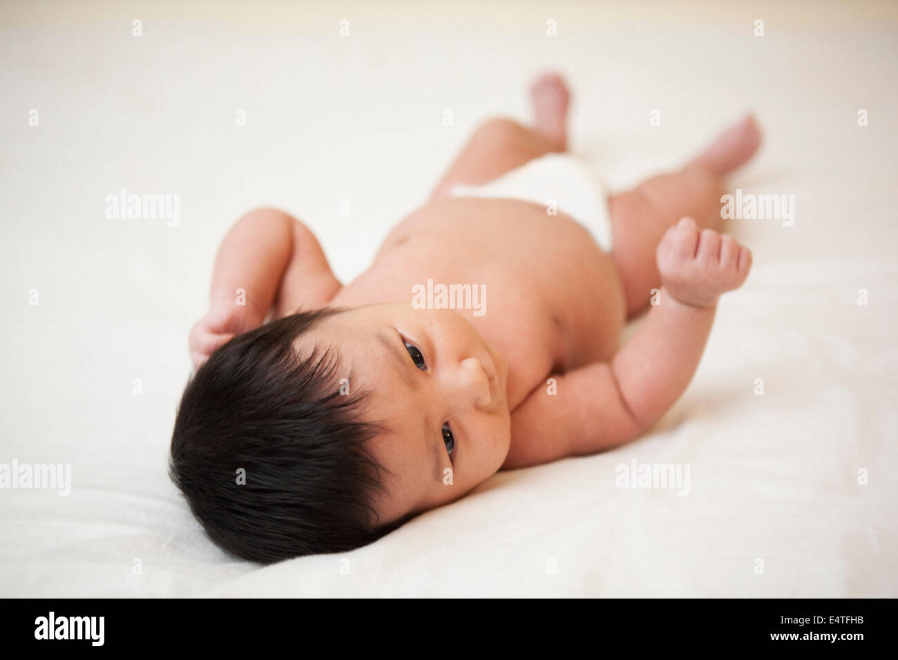 Newborn Asian baby in diaper lying on back, scratching head from baby acne, studio shot on white background Stock Photo