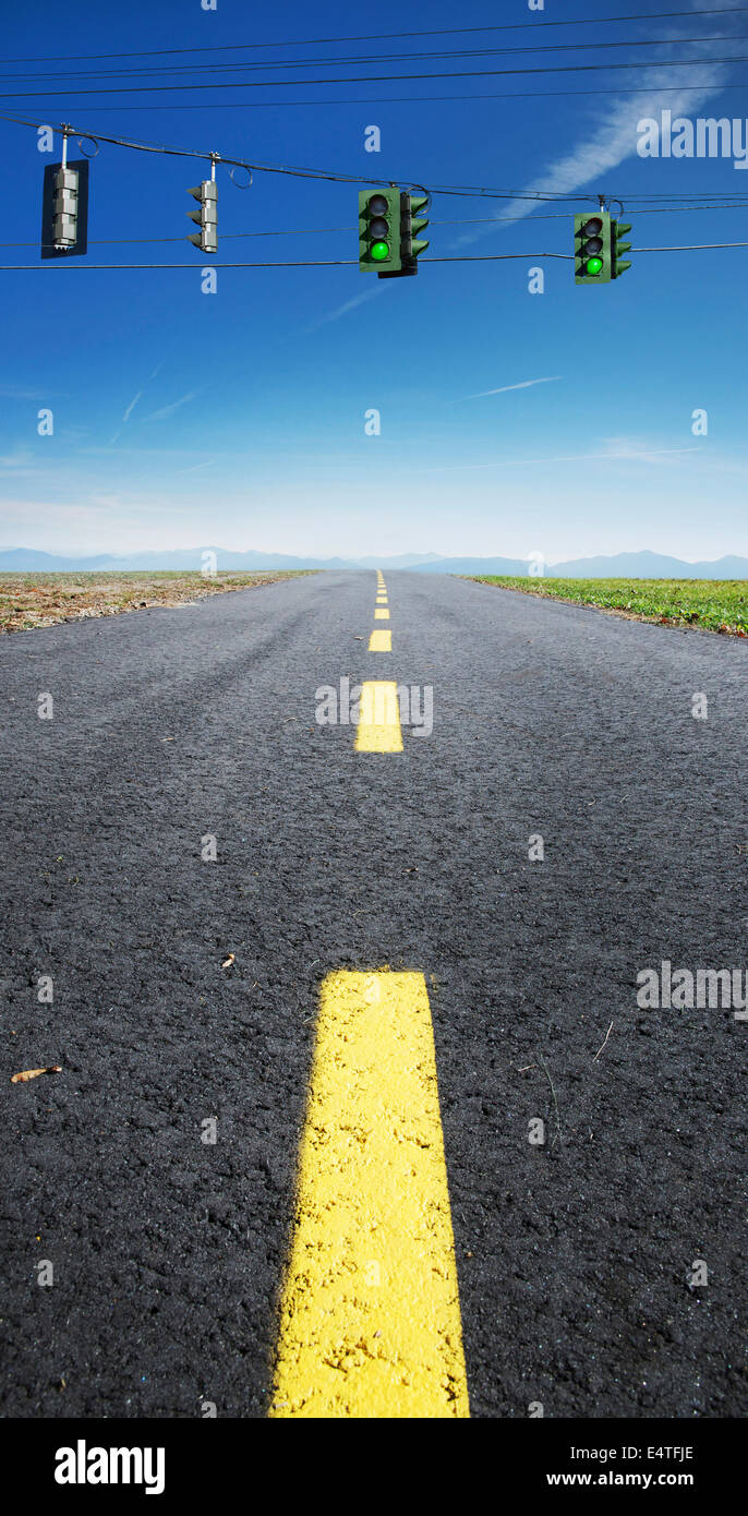 Closeup view of yellow, broken center line on deserted highway, with red traffic lights hanging