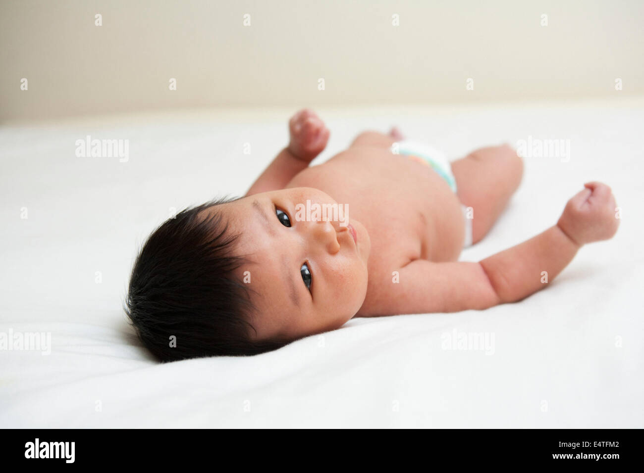 Newborn Asian baby in diaper, looking up at camera, studio shot on white background Stock Photo