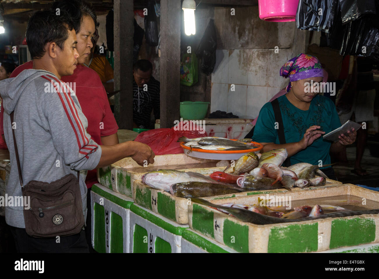 Bali, Indonesia.  Jimbaran Fish Market.  Woman Calculating Price of Fish for Two Buyers. Stock Photo