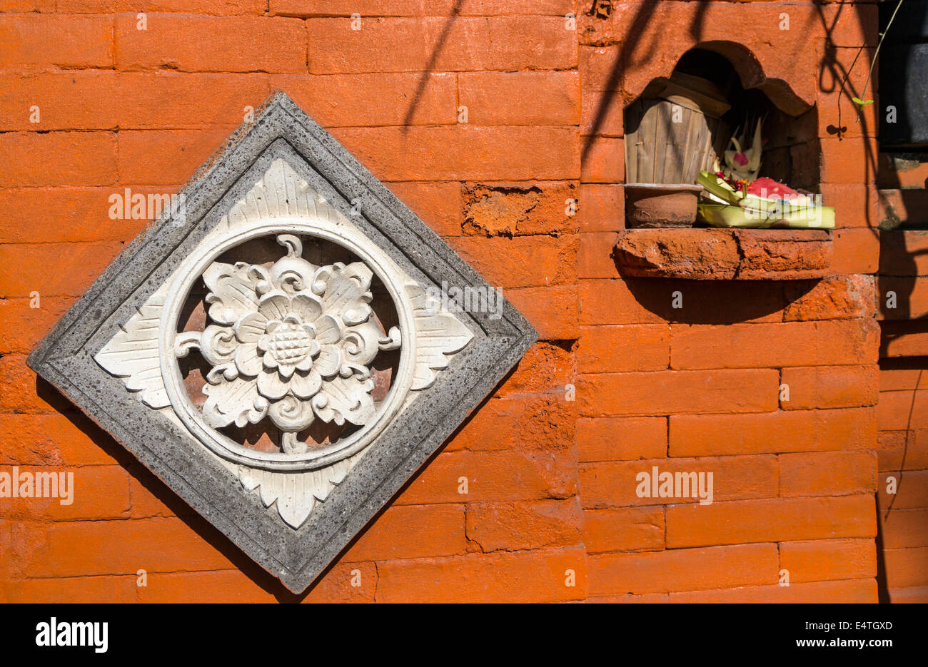 Jimbaran, Bali, Indonesia.  Offerings (Canang) in a Wall Recess Adjacent to Entrance to a Restaurant.  Lotus Flower Decoration. Stock Photo