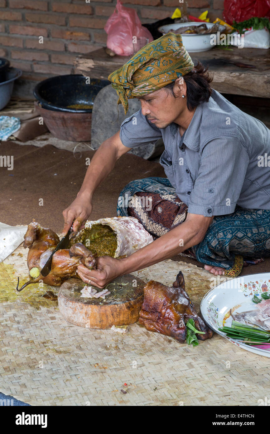 Bali, Indonesia.  Roasted Pig Being Cut up by Village Cook.  He is wearing the udeng, the traditional Balinese head cloth. Stock Photo
