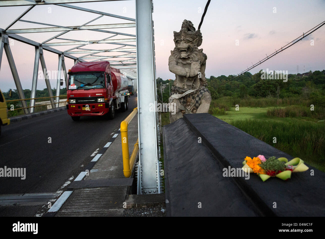 Bali, Indonesia.  Mythical Hindu Figure Guards a Bridge in Southern Bali.  Offering Basket (Canang) in Foreground. Stock Photo
