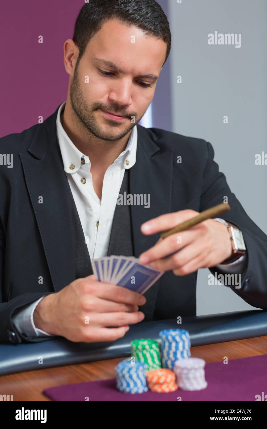 Man holding a cigar looking at his cards Stock Photo