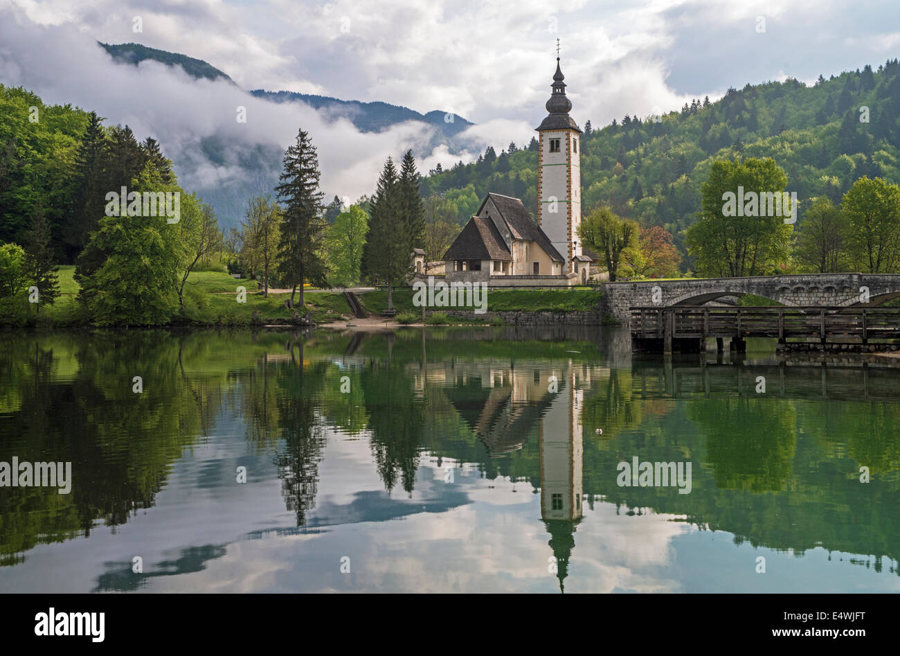 Church reflected in the calm waters of Lake Bohinj in Slovenia early one morning Stock Photo