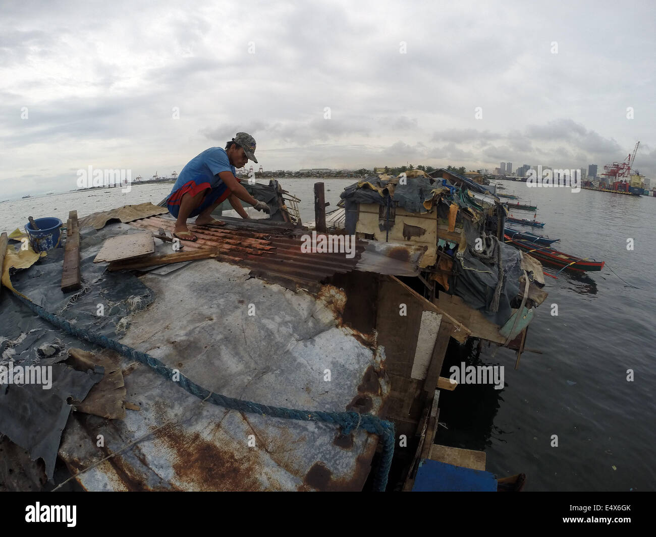 Manila, Philippines. 17th July, 2014. A man repairs the roof of his home after it was damaged by typhoon Rammasun at a slum area in Manila, the Philippines, on July 17, 2014. The death toll from typhoon Rammasun rose to 38, the local disaster agency said Thursday. The National Disaster Risk Reduction and Management Council (NDRRMC) said the typhoon also left 10 people injured while eight others were declared missing. Credit:  Rouelle Umali/Xinhua/Alamy Live News Stock Photo