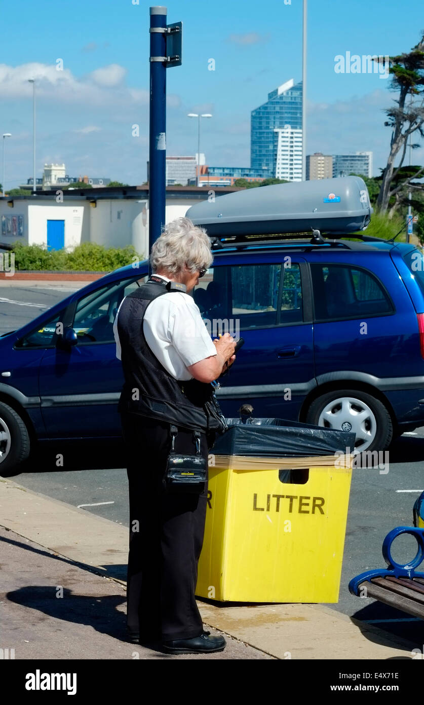 a traffic warden takes down a parked cars details on the seafront on a hot sunny day in southsea uk Stock Photo
