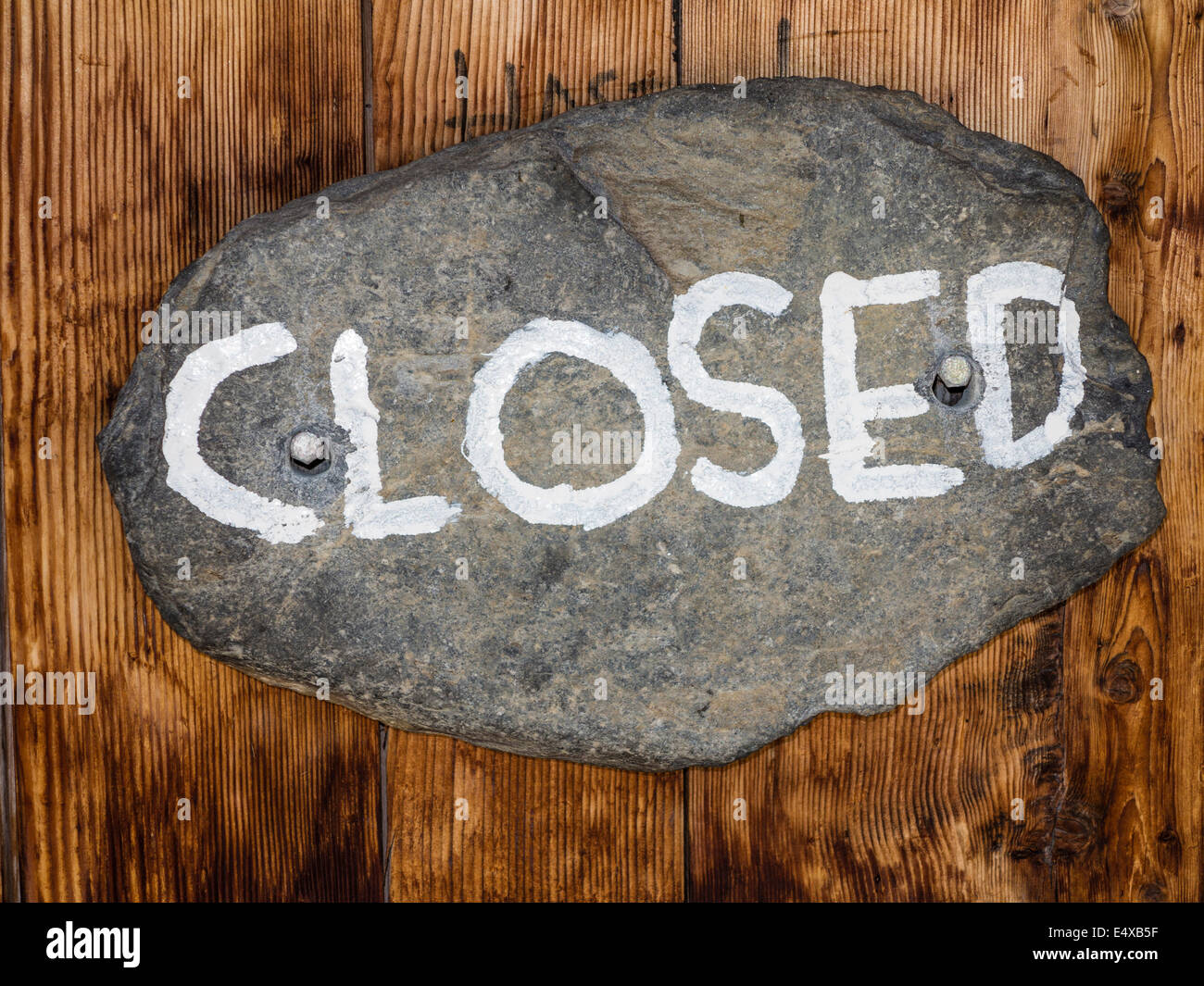 The sign 'closed', written on an oval stone, nailed to a wooden door Stock Photo