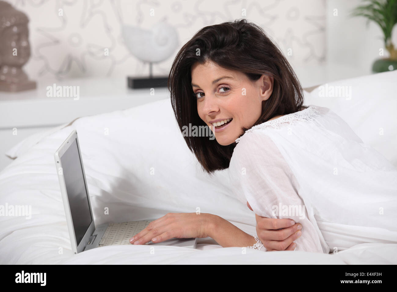 Woman using laptop lying on a bed Stock Photo - Alamy