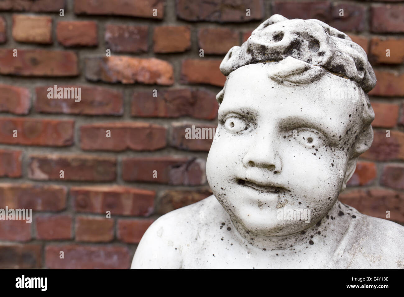 An old white marble statue of a cherub boy against a garden wall with