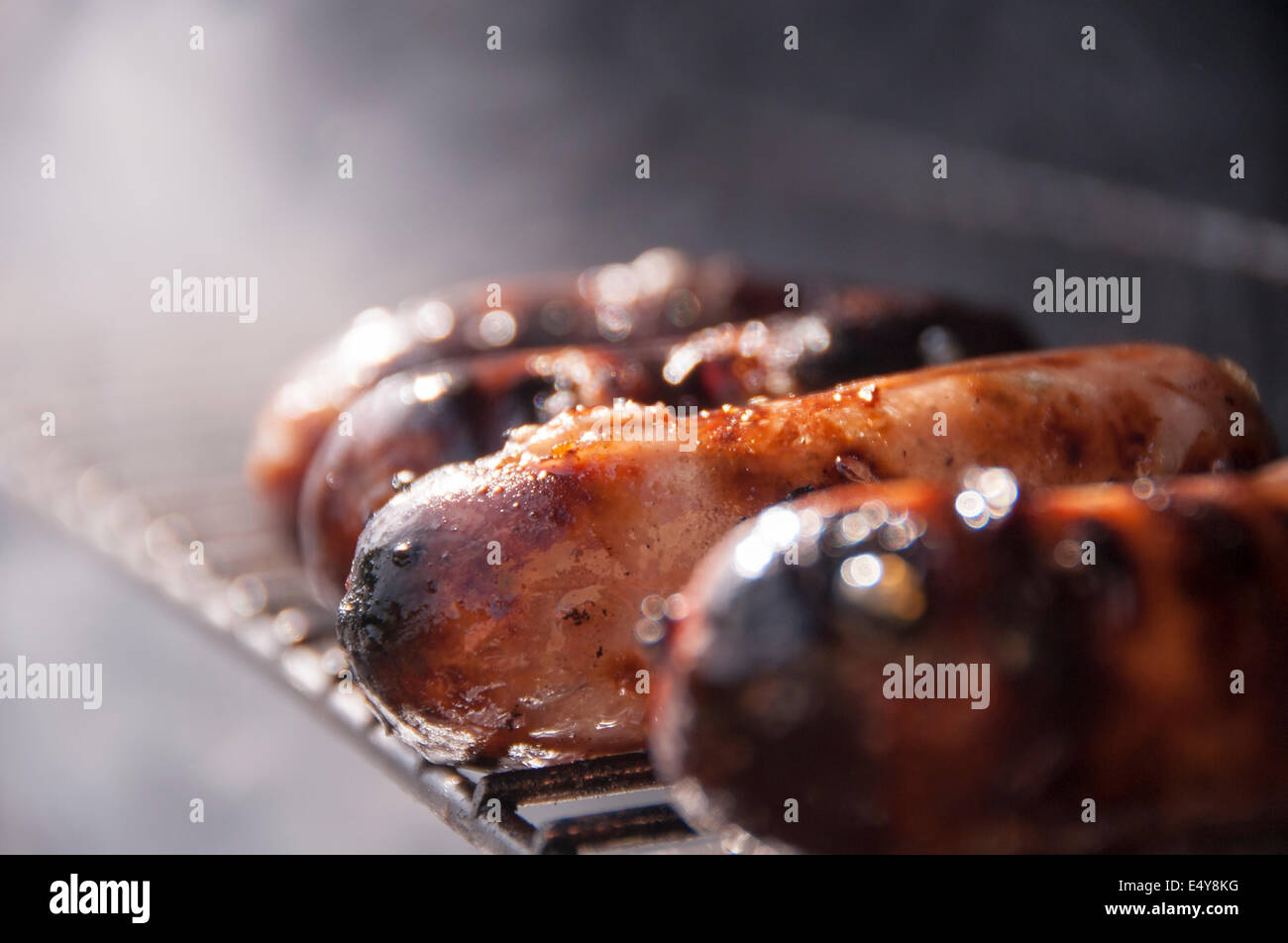 Sausages cooking on a bbq grill, sizzling and smoking away in the sunshine Stock Photo
