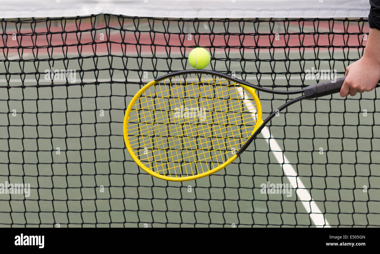 Horizontal photo of a tennis racket in front of ball with net and court in background Stock Photo