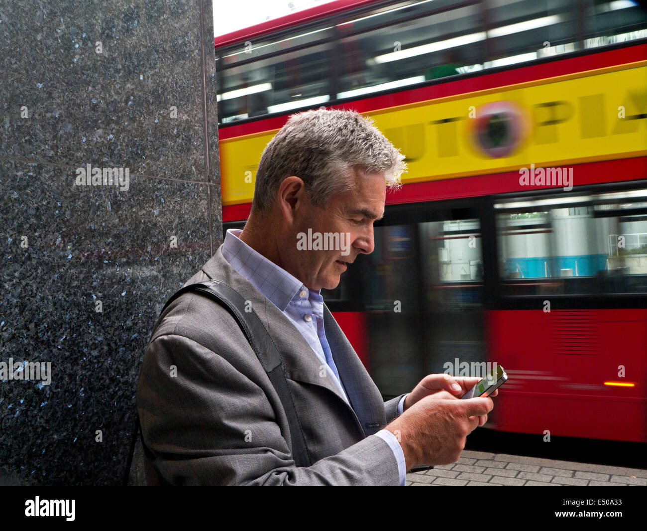 Mature businessman using an iPhone smartphone in London Southbank with blurred traditional London red bus passing in background Stock Photo