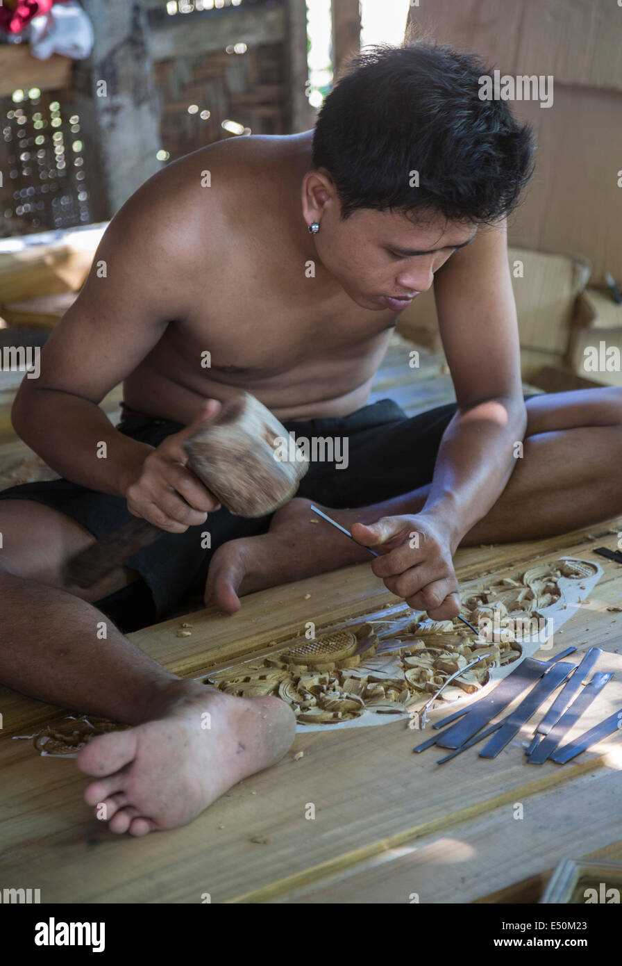 Bali, Indonesia.  Woodcarver Carving Design into Door Frame in Woodworker's Workshop. Stock Photo